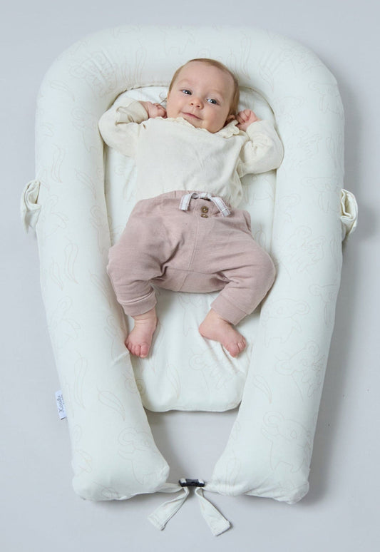Baby lying in a white baby nest on a light gray background